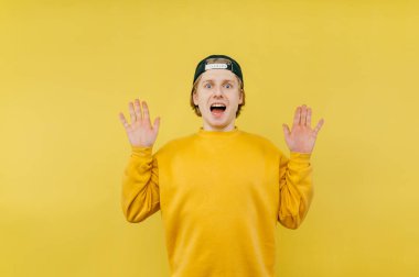 Şok olmuş genç adam, kollarını kaldırdı avuç içlerini kaldırdı ve sarı arka planda duygusal bir yüzle kameraya baktı..