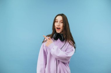 Mutlu yüzlü komik bir kadın parmağıyla fotokopi makinesini işaret ediyor ve kulaklığa kazak takmış kameraya bakıyor. Mavi bir arkaplanda izole edilmiş