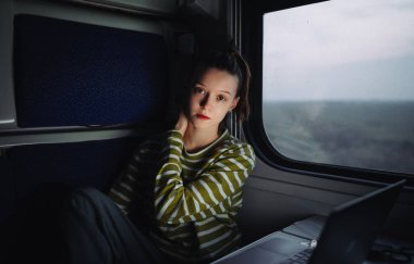 Çekici kadın turistin portresi trende dizüstü bilgisayarla geziyor ve ciddi bir yüzle kameraya poz veriyor..