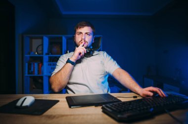 Düşünceli erkek rötuşçu gece bilgisayar başında çalışıyor ve ekrana bakıyor ve ciddi bir yüz ve düşünüyor.