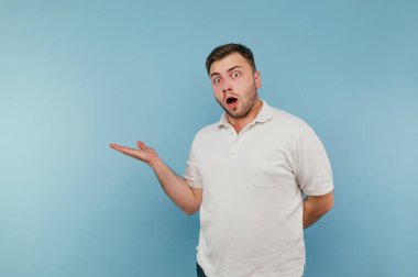 Mavi arka planda beyaz tişörtlü, şaşırmış bir adamın portresi. Şok olmuş bir yüzle kameraya bakar ve fotokopi çekerken elini yana çevirir.