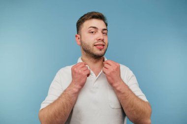 Beyaz tişörtlü, yüzünde mavi bir gülümsemeyle kameraya poz veren sevimli bir adam..