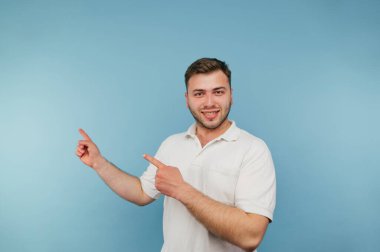 Mavi arka planda beyaz tişörtlü olumlu bir adam yüzünde bir gülümsemeyle kameraya bakar ve boş bir alanda yüzünü gösterir..