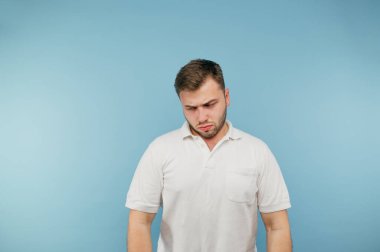 Mavi arka planda tüyleri olan, beyaz tişörtlü, başarısızlıktan başı öne eğilmiş üzgün bir adamın portresi..