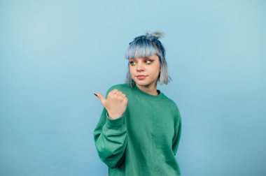 Mavi saçlı ve ciddi yüzlü güzel bir kız mavi bir arka planda duruyor ve fotokopi alanının kenarına bakıyor.