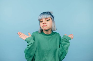 Mavi arka planda kafası karışmış bir yeniyetme kızın portresi, kameraya şaşkın şaşkın bakıyor..