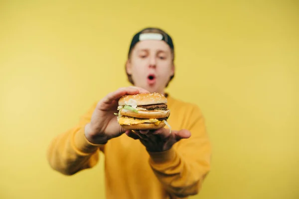 Шокированный Позитивный Молодой Человек Держит Руках Аппетитный Бургер Показывает Камеру — стоковое фото