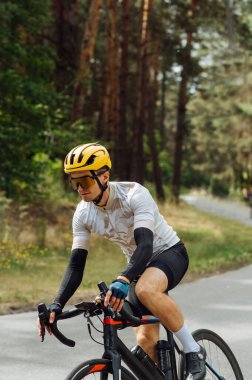 Bisikletli bir adamın dikey fotoğrafı ormanın arka planında ciddi bir yüzü olan bir bisiklete biniyor. Bisiklet üstünde antrenman