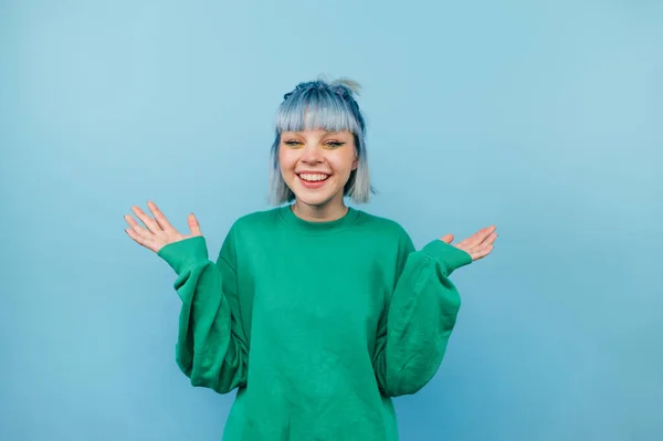 ポジティブなティーン女の子とともに青い髪と緑のセーター喜びで上げ手上の色の背景 — ストック写真