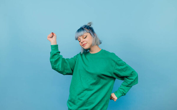 Cute teen girl with colored hair dancing with a smile on his face on a blue background and closed eyes.