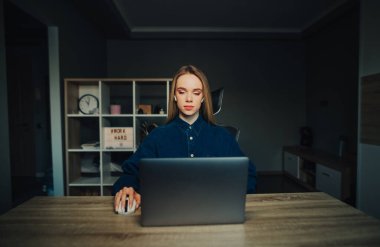 Kablosuz kulaklıklı güzel bir kadın. Evde, masada oturuyor ve ciddi bir yüzle dizüstü bilgisayarla çalışıyor..