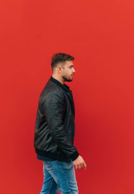 Ceketli sakallı bir adam kırmızı bir duvarın arka planında yürür..