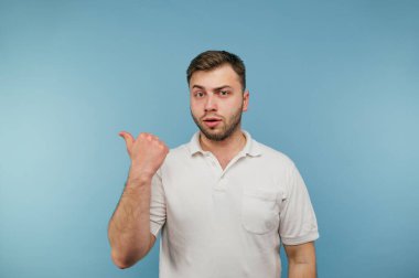 Mavi arka planda duran beyaz tişörtlü yakışıklı adam ciddi bir yüz ve fotokopi alanını gösteren parmaklar.