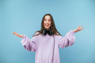 Mor kazaklı neşeli kadın mavi bir arka planda duruyor ve yüzünde bir gülümsemeyle kameraya neşeli bir şekilde bakıyor..