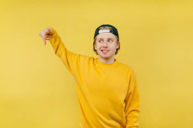 Şapkalı olumlu bir adam sarı arka planda duruyor ve yüzünde bir gülümsemeyle fotokopi alanının kenarını işaret ediyor..