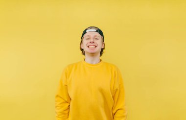 Sarı arka planda şapkalı, sevimli, pozitif bir adamın portresi yüzünde bir gülümsemeyle kameraya bakıyor ve dişlerini gösteriyor..