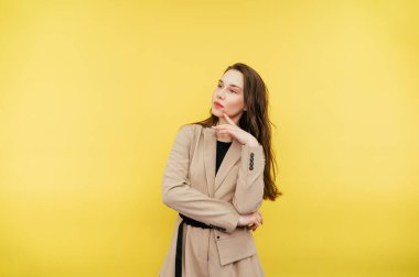 Ceketli düşünceli iş kadını sarı arka planda duruyor ve kafasını çeviriyor..