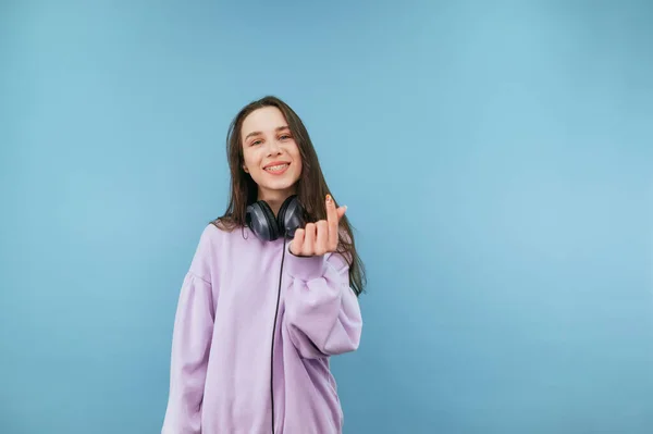 Pozitivní Dívka Sluchátkách Stojí Modrém Pozadí Sluchátkách Ukazuje Srdeční Gesto — Stock fotografie