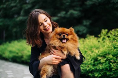 Çekici esmer bir kadının portresi. Kollarında şirin bir Pomeranya köpeğiyle bir evcil hayvana bakıyor ve gülümsüyor..