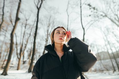 Ceketli şık bayan kış ormanlarında kameraya poz veriyor ve ciddi bir yüz ifadesiyle başka yere bakıyor..