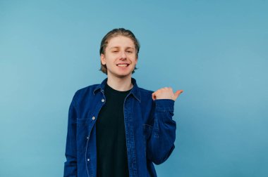 Yüzünde bir gülümseme olan genç adam kameraya bakar ve parmağını yana çevirir..