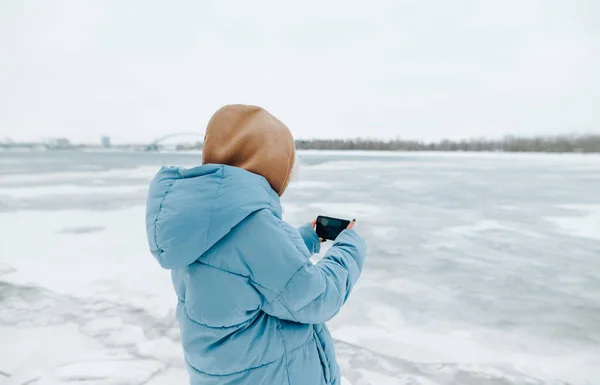 Dívka Turista Teplé Bundě Stojí Břehu Zamrzlého Jezera Fotí Smartphone — Stock fotografie