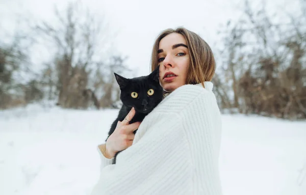 스웨터를 겨울에 눈덮인 거리를 귀여운 여성의 과검은 고양이를 — 스톡 사진