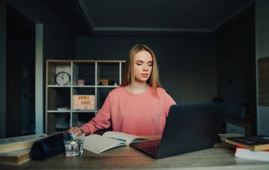 Güzel öğrenci kız evde uzaktan çalışıyor, rahat bir odada bir masada oturuyor..