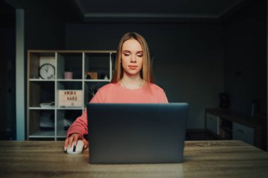 Evde dizüstü bilgisayarla çalışan çekici genç bir kadın. Ciddi bir yüzü var..