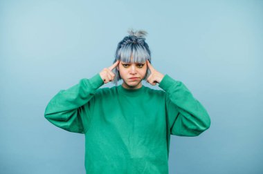 Siyah saçlı düşünceli genç kız mavi bir arka planda duruyor. Ciddi bir yüzü var, parmaklarını şakağına gösteriyor..