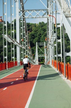 Spor kıyafetli bisikletçi, ormanın arka planında, dikey bir köprüde bisiklet sürüyor..