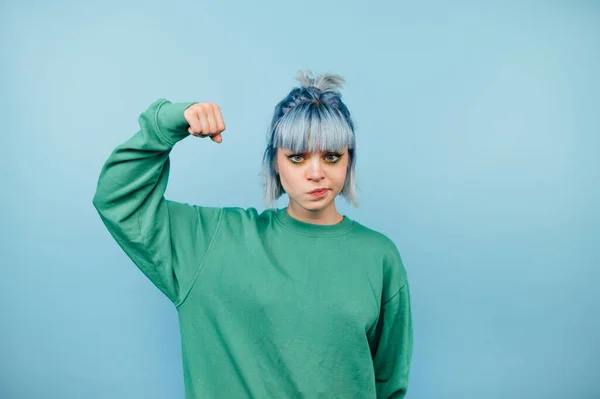 Seriózní Teen Dívka Zelené Mikině Stojí Modrém Pozadí Ukazuje Biceps — Stock fotografie