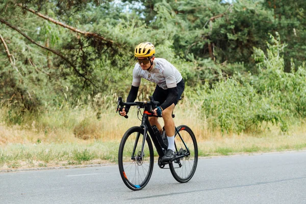 A guy in sportswear rides a bicycle on a country road in the woods.