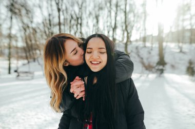 Parkta kış yürüyüşü sırasında yüzlerinde bir gülümsemeyle sarılan en iyi iki arkadaş.