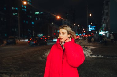 Kırmızı ceketli güzel bir kadın gece karlı bir sokakta yürüyor, yüzünde bir gülümsemeyle başka yere bakıyor..