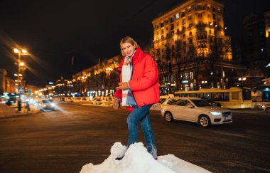 Karlı bir şehrin arka planında kameraya bakıp gülen gülümseyen bir kadın..
