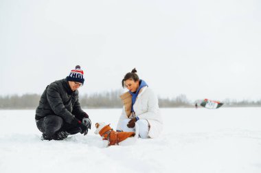 Kış yürüyüşü sırasında bir Jack Russell köpeğiyle karda oturmuş bir evcil hayvana bakıyor ve gülümsüyor..