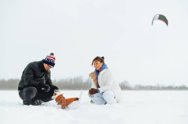 Güzel bir köpekle yürüyüşe çıkmış mutlu bir çift karlı bir tarlada oturuyor ve yüzünde gülümseme olan bir evcil hayvanla oynuyor..