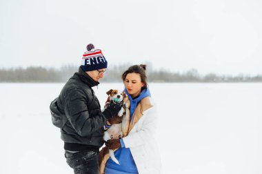 Güzel bir kadının portresi. Kocası kışın karlı zeminde duruyor. Elinde küçük sevimli bir köpekle..