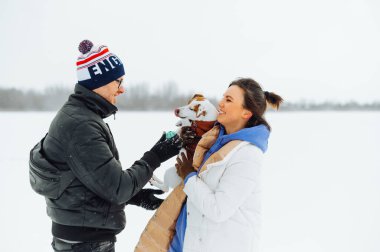 Sıradan giyinmiş bir adamla pozitif bir kadın kış yürüyüşünde bir evcil hayvanla vakit geçirir. Kollarında bir köpek tutar ve gülümserdi..