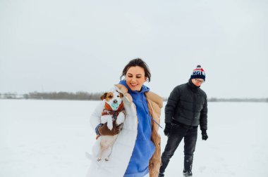 Küçük sevimli bir köpekle karlı bir gölde yürüyüş yapan mutlu bir aile..