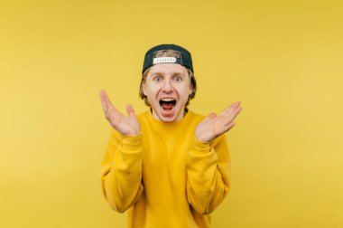 Şapkalı neşeli genç adam sarı bir arka planda duruyor ve mutlu bir şekilde kameraya bakıyor..
