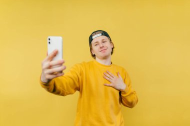 Şapkalı ve günlük kıyafetli neşeli bir adam sarı arka plandaki akıllı telefon kamerasından selfie çeker ve güler..