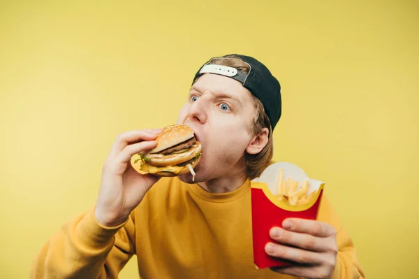 Funny Hungry Guy Cap Bites Burger Holds French Fries Looking — стоковое фото