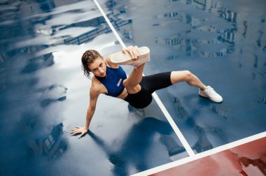 Mavi spor kıyafetli güzel bir kadın sokakta spor yapıyor, ıslak bir zeminde yağmurlu havada esneme hareketleri yapıyor..