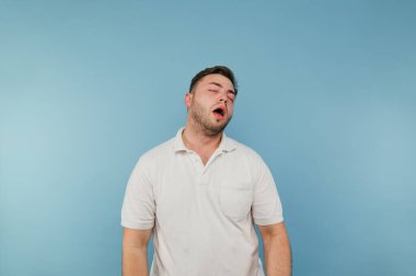 Beyaz tişörtlü yorgun adam mavi arka planda uyuyor..