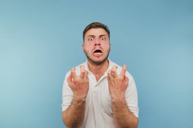 Beyaz tişörtlü kızgın adam duygusal olarak gergin ve mavi arka planda bağırıyor..