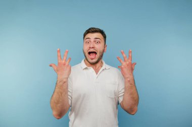 Beyaz tişörtlü neşeli adam ellerini kaldırdı. Mavi arka planda sevinçler ve bağırışlar..