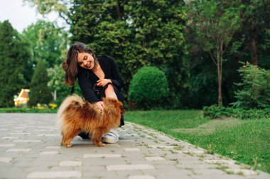 Parkta tatlı bir köpeğiyle yürüyen pozitif kadın ve gülümsüyor..