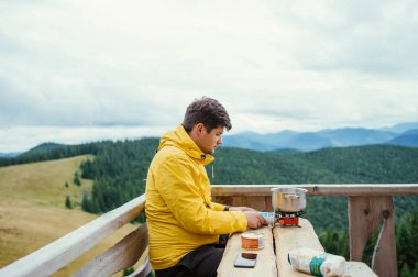 Ceketli bir erkek turist, bir kır evinin terasında ocakta yemek yemeye hazırlanıyor.